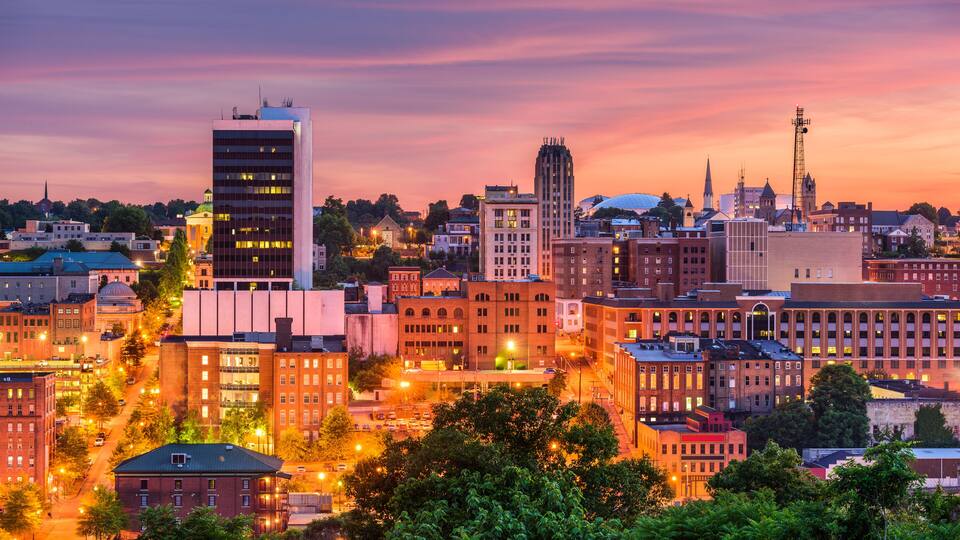 A cityscape at dusk with illuminated buildings and a church steeple.