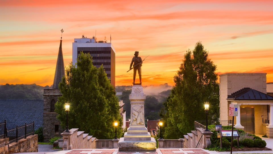 A statue in a plaza with a sunset sky, surrounded by trees and buildings.