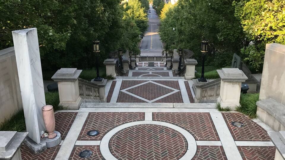 A grand staircase leading up to a patterned plaza surrounded by trees and buildings.
