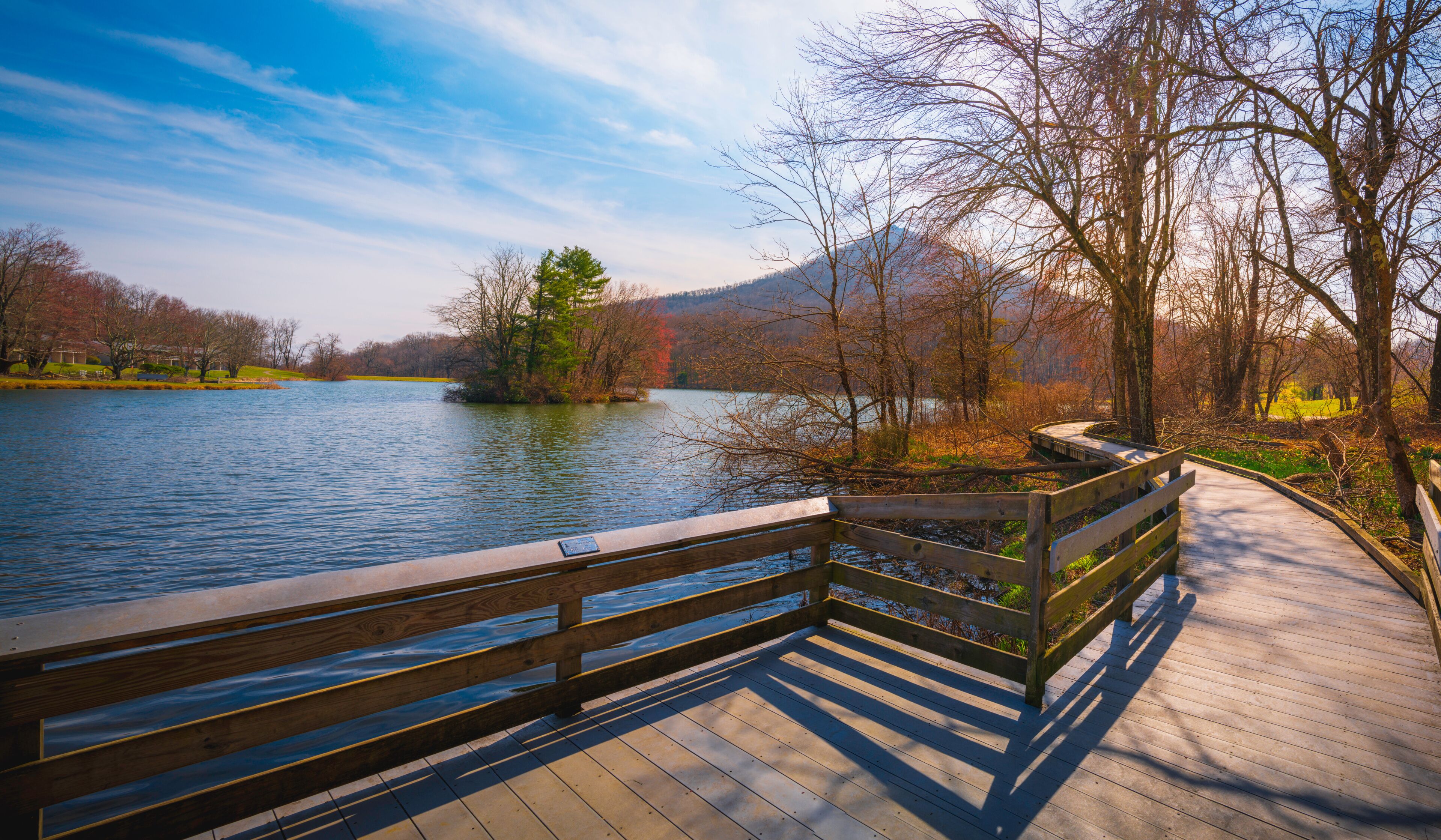 Tranquil spring nature landscape of Blue Ridge Mountains and Peaks of Otter Lake on the Blue Ridge Parkway in Bedford, Virginia, USA, boardwalk footpath, green and res sprouts and water reflections