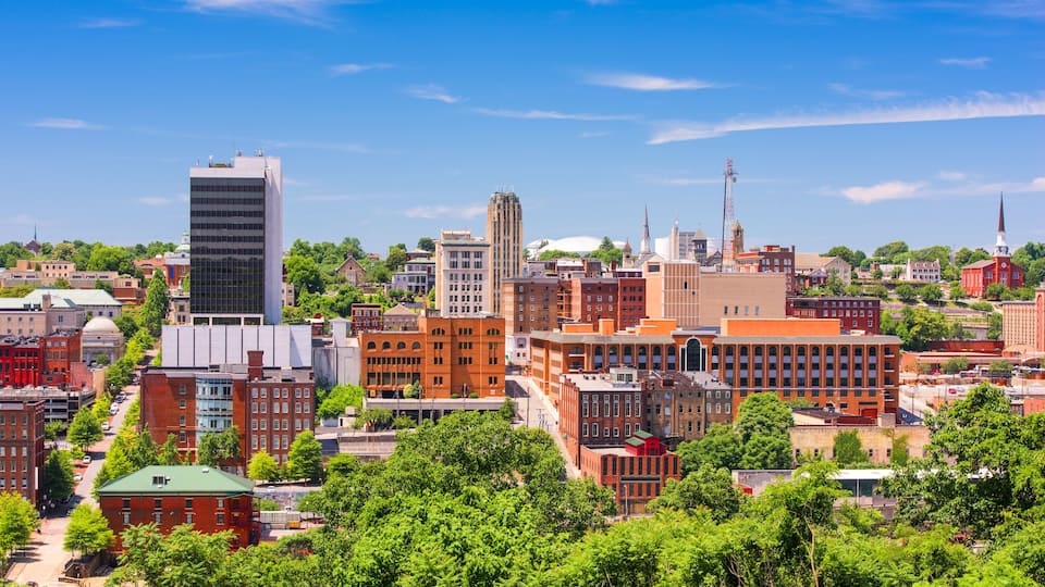 A cityscape with a mix of modern and historic buildings, a prominent church steeple, and lush green trees.