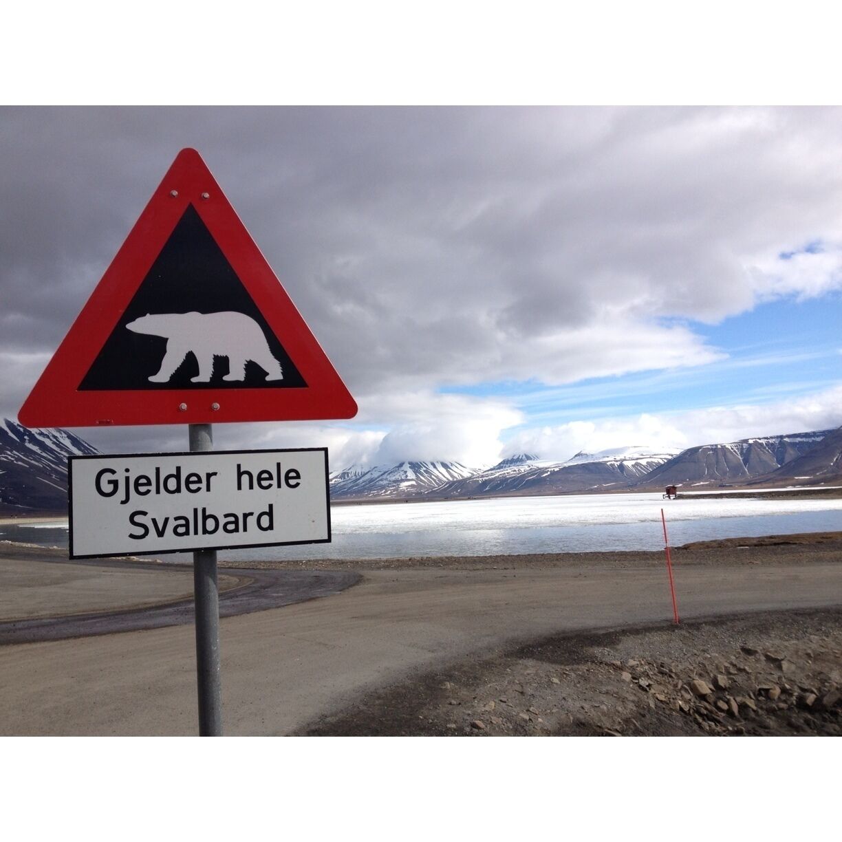 A polar bear crossing sign with a landscape of mountains and a lake in the background.