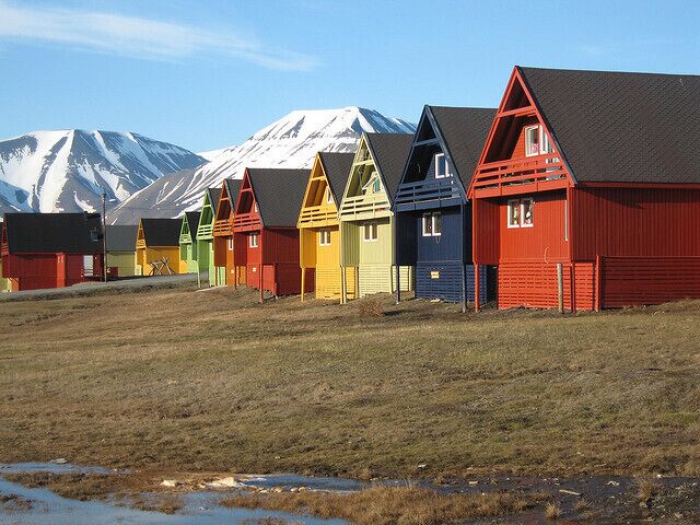 Colorful wooden houses with snow-capped mountains in the background.