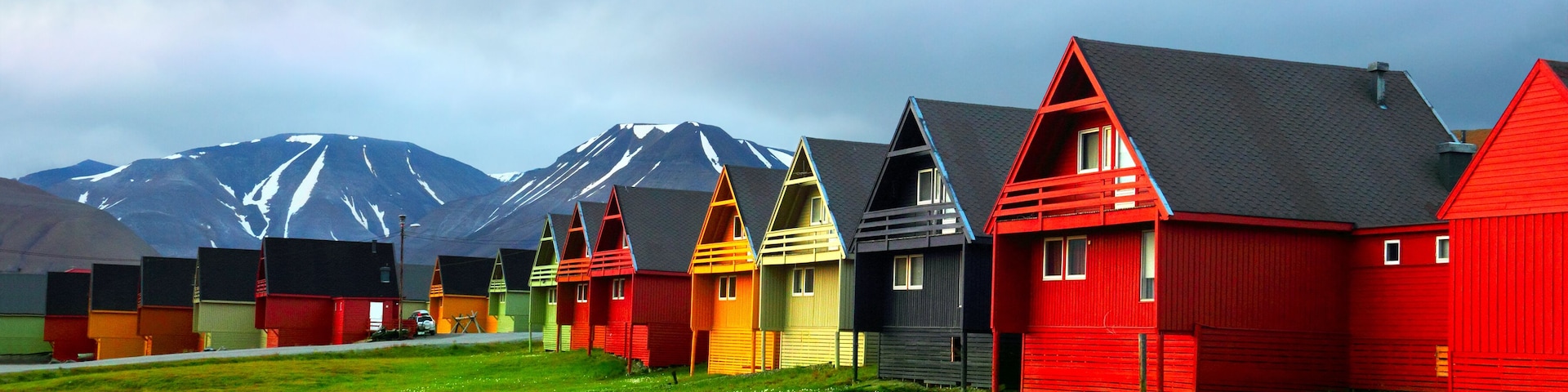 Idyllic scenic view, colorful houses and green field with arctic flowers against the background of dramatic sky and barren mountain in Longyearbyen, Spitsbergen archipelago (Svalbard), Norway, Europe