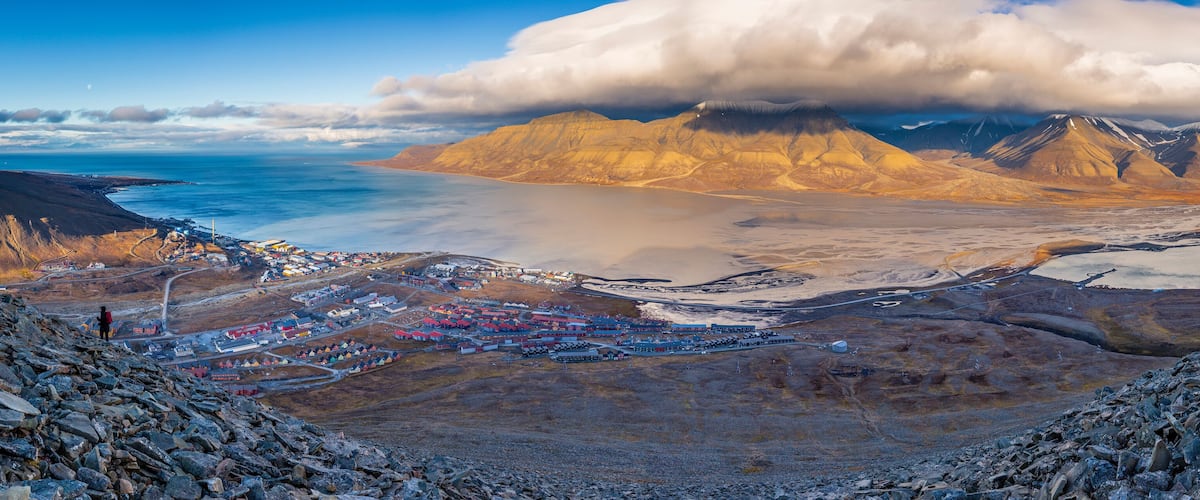 A coastal town with colorful buildings, a large mountain range, and a body of water.