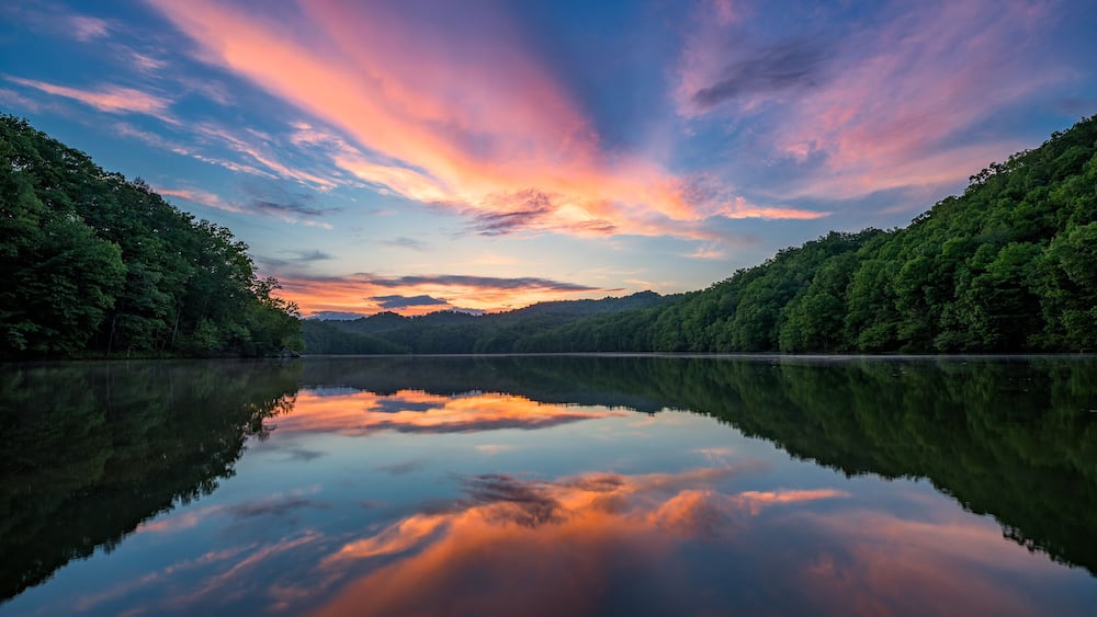 A calm lake with a reflection of the sky, surrounded by dense forest.