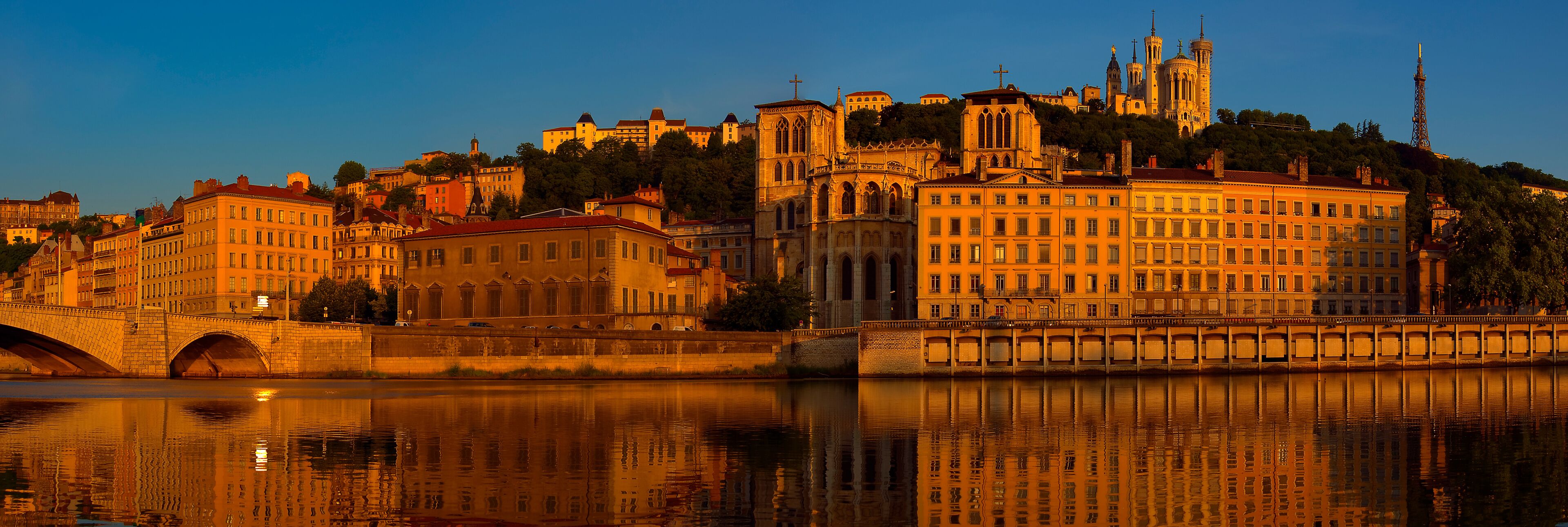 A cityscape with a prominent cathedral, a bridge, and a river reflecting the buildings.