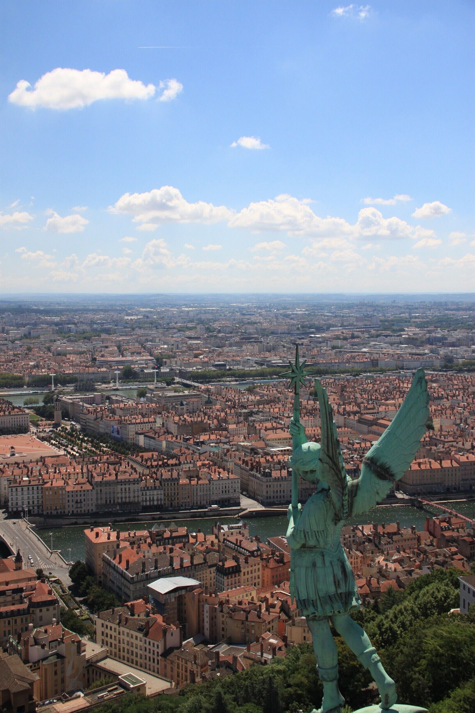 Uma estátua de uma figura alada com vista para a paisagem urbana, com um rio e edifícios históricos.