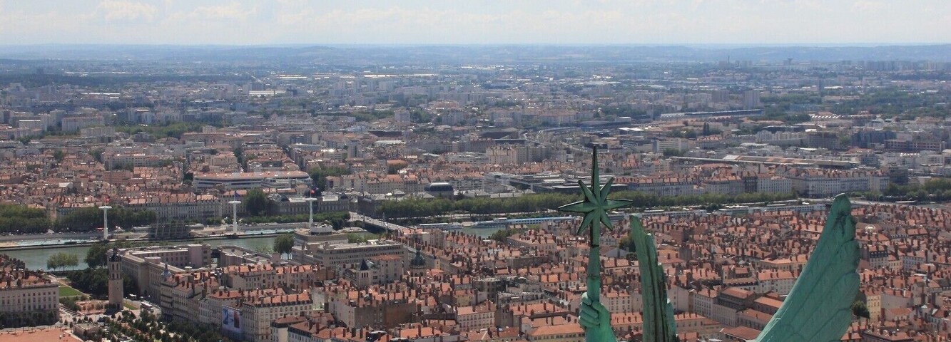 Uma estátua de uma figura alada com vista para a paisagem urbana, com um rio e edifícios históricos.