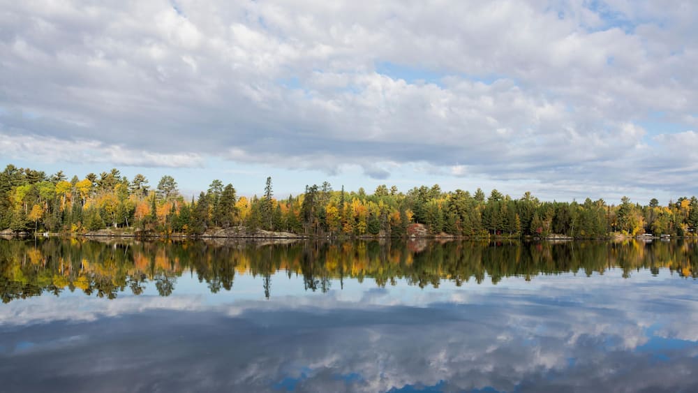 HM6T3R Scenic view of trees and cloudy sky reflecting on calm lake during autumn
