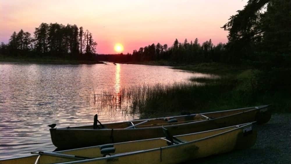 A sunset over a calm lake with canoes lined up on the shore.