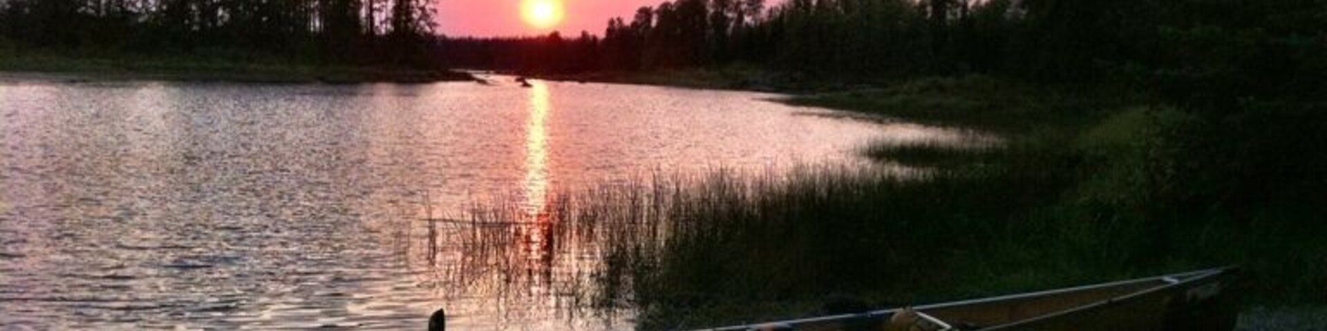 A sunset over a calm lake with canoes lined up on the shore.