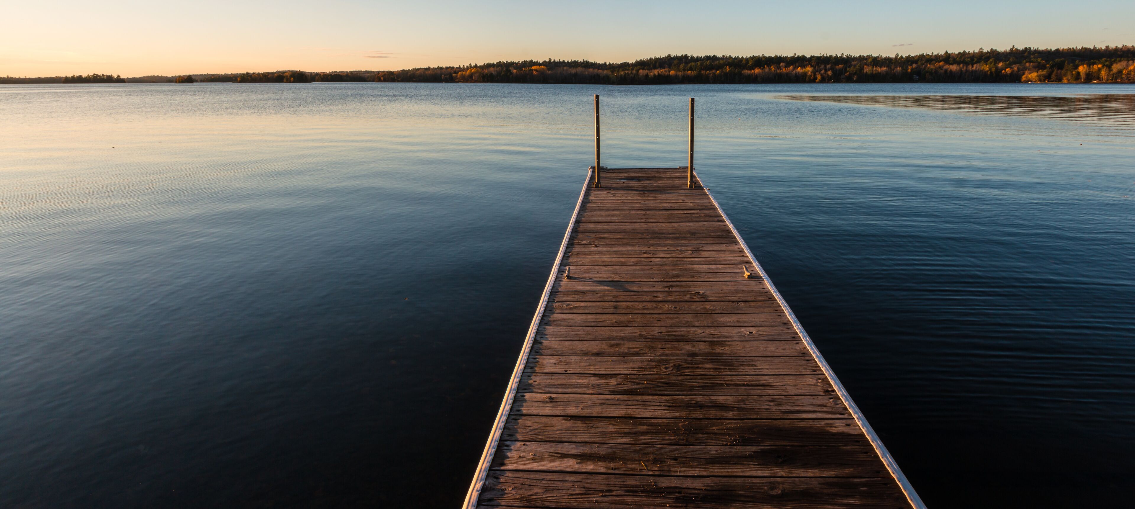 A wooden pier extending into calm water with a forested shoreline in the background.