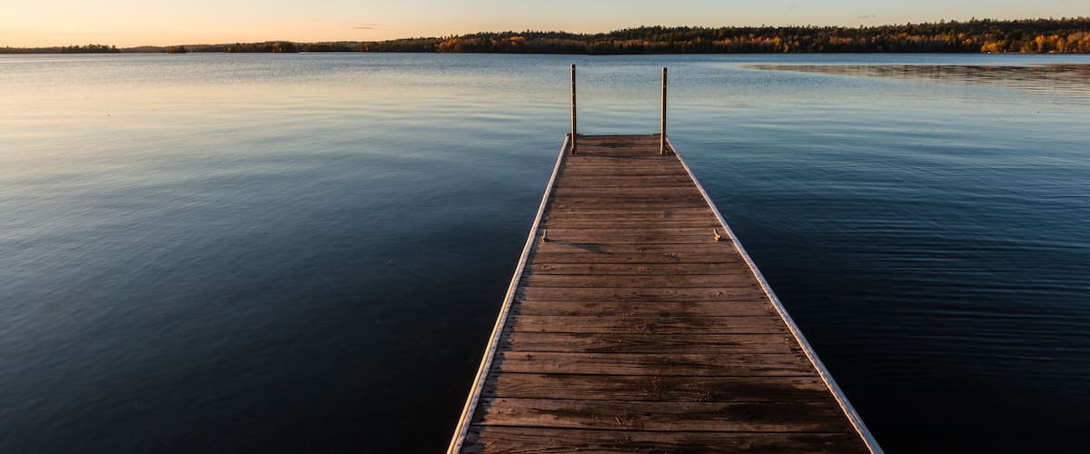 A wooden pier extending into calm water with a forested shoreline in the background.
