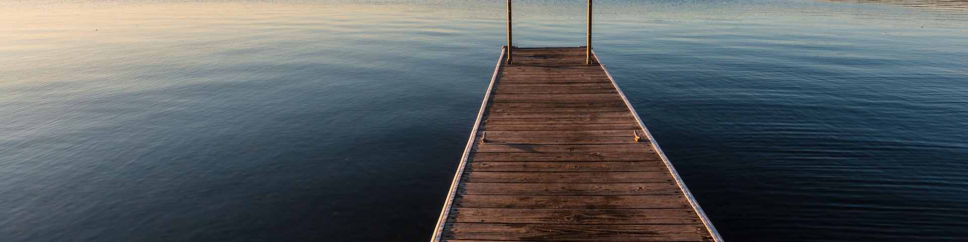 A wooden pier extending into calm water with a forested shoreline in the background.