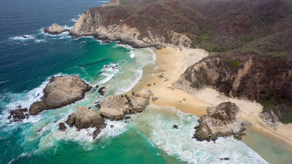 A coastal landscape with rocky cliffs, a sandy beach, and turquoise waters.