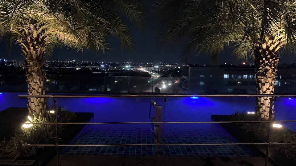 A nighttime view of a pool area with palm trees and a cityscape in the background.