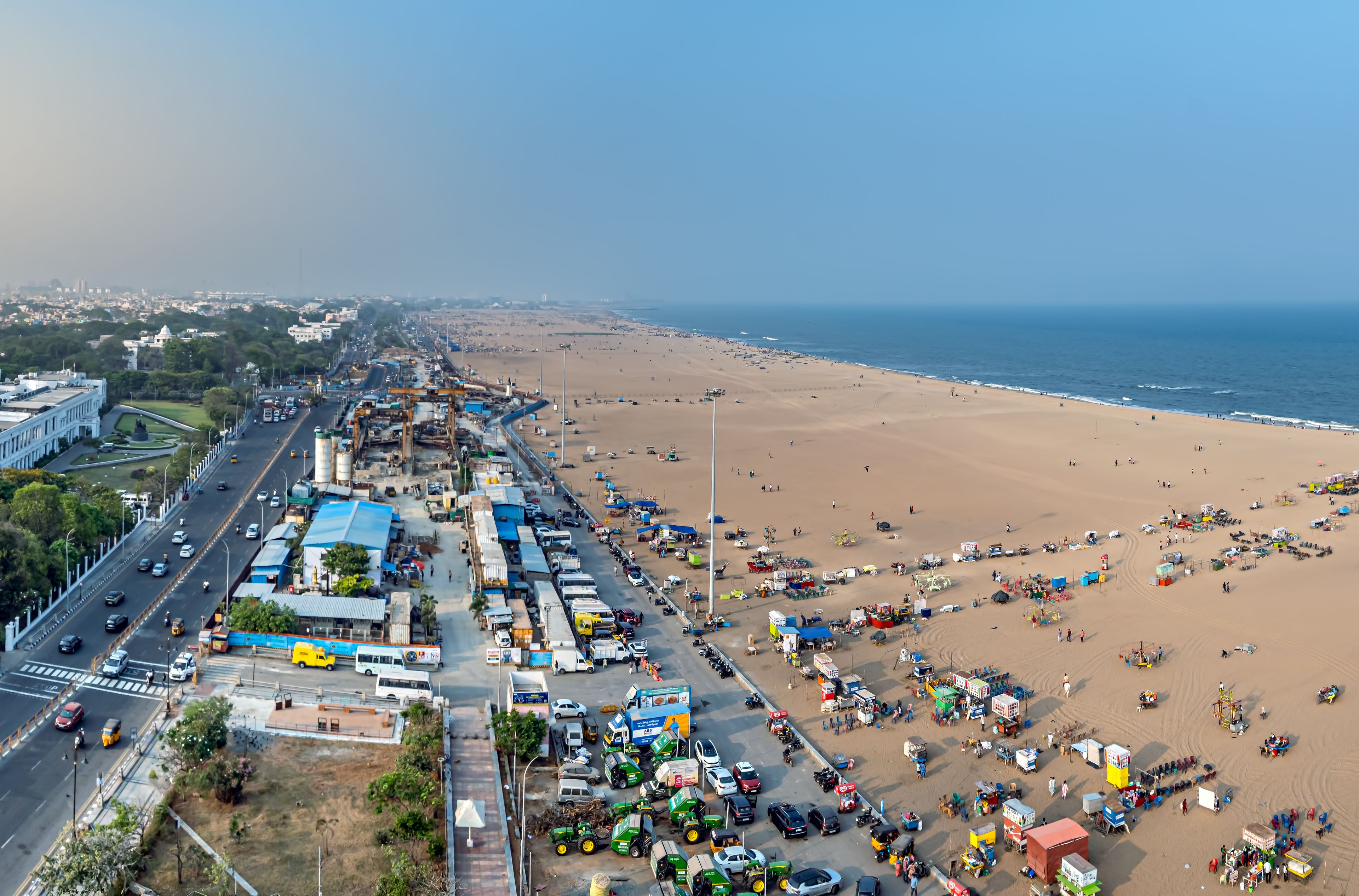 Un paysage urbain côtier avec une plage animée, une autoroute et des bâtiments industriels.