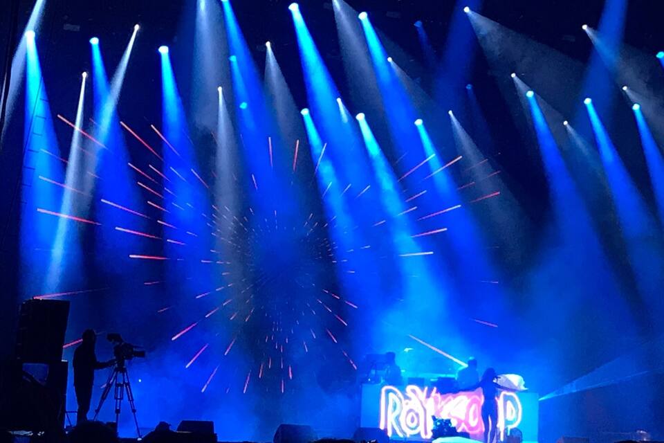 A stage with blue and pink lights, a DJ booth, and a crowd.