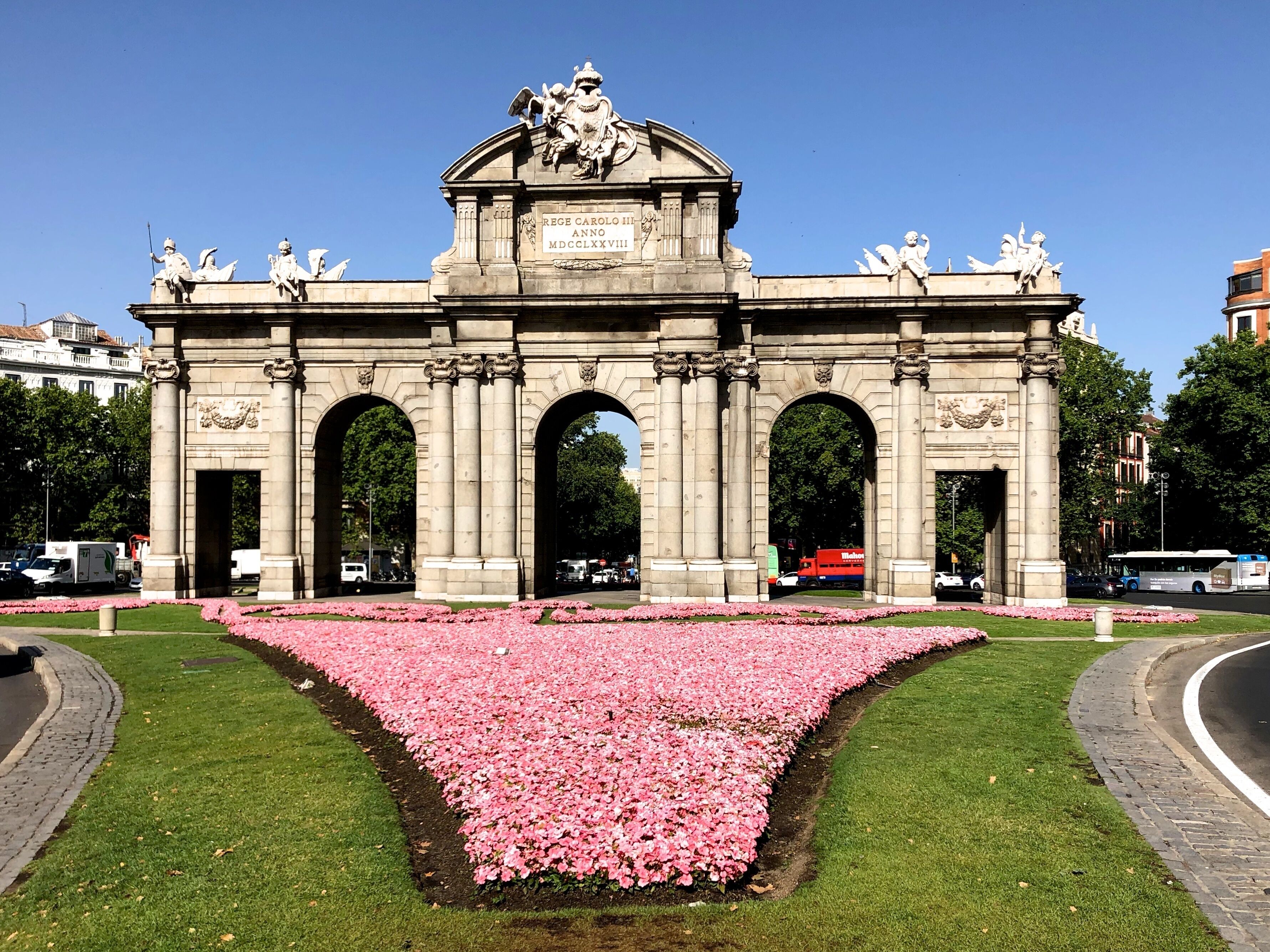 Erected in 1778 by Italian architect Francesco Sabatini, this triumphal gate was once the main entrance to the city. It was commissioned by King Charles III - over time nicknamed the Best Mayor of Madrid -, who was unimpressed by the gate that welcomed him when he first arrived in 1759. It is situated next to El Retiro Park in the centre of Plaza de la Independencia, a junction for three of the city’s most well-known streets: Calle de Alcalá, the city’s longest road, Calle de Alfonso XII, which leads to Atocha train station, and Calle de Serrano, Madrid’s most glamorous thoroughfare.

Designed by Sabatini, Puerta de Alcalá is a neoclassical triumphal arch made of granite. It was the first of its kind to be built after the fall of the Roman Empire, making it even older than Berlin’s Brandenburg Gate or the Arc de Triomphe in Paris. Unlike the smaller Puerta de Toledo and Puerta de San Vicente gates, which are also located in the centre of the city, Puerta de Alcalá has a total of five arches, not three.

Each side of the gate has a different design. The one looking towards the city centre is crowned by sculptures of war trophies such as flags, weapons, breastplates and helmets, and its three rounded arches are decorated with the head of a lion. The other side, which is the one travellers would first behold when they arrived in the city, is more ornately decorated and is crowned by the royal coat of arms held up by Fame helped by a child. Along the top of the gate, you’ll find the figures of four children that are an allegory of the cardinal virtues: fortitude, justice, temperance and prudence.

The gate was given the name Puerta de Alcalá because it was on the road that led to Alcalá de Henares, Cervantes’ hometown.