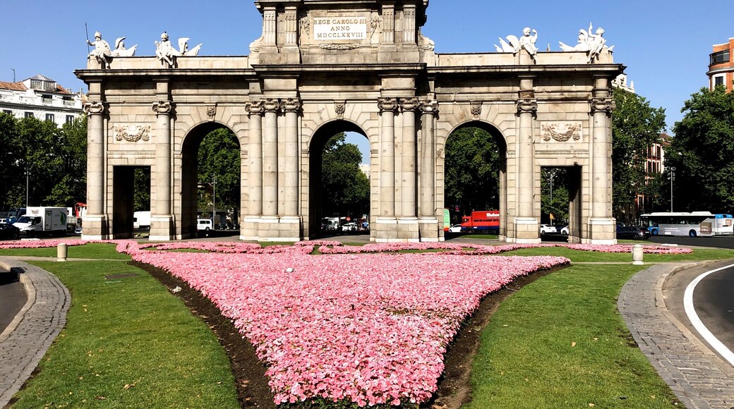 Erected in 1778 by Italian architect Francesco Sabatini, this triumphal gate was once the main entrance to the city. It was commissioned by King Charles III - over time nicknamed the Best Mayor of Madrid -, who was unimpressed by the gate that welcomed him when he first arrived in 1759. It is situated next to El Retiro Park in the centre of Plaza de la Independencia, a junction for three of the cityâs most well-known streets: Calle de AlcalĂĄ, the cityâs longest road, Calle de Alfonso XII, which leads to Atocha train station, and Calle de Serrano, Madridâs most glamorous thoroughfare.
Designed by Sabatini, Puerta de AlcalĂĄ is a neoclassical triumphal arch made of granite. It was the first of its kind to be built after the fall of the Roman Empire, making it even older than Berlinâs Brandenburg Gate or the Arc de Triomphe in Paris. Unlike the smaller Puerta de Toledo and Puerta de San Vicente gates, which are also located in the centre of the city, Puerta de AlcalĂĄ has a total of five arches, not three.
Each side of the gate has a different design. The one looking towards the city centre is crowned by sculptures of war trophies such as flags, weapons, breastplates and helmets, and its three rounded arches are decorated with the head of a lion. The other side, which is the one travellers would first behold when they arrived in the city, is more ornately decorated and is crowned by the royal coat of arms held up by Fame helped by a child. Along the top of the gate, youâll find the figures of four children that are an allegory of the cardinal virtues: fortitude, justice, temperance and prudence.
The gate was given the name Puerta de AlcalĂĄ because it was on the road that led to AlcalĂĄ de Henares, Cervantesâ hometown.