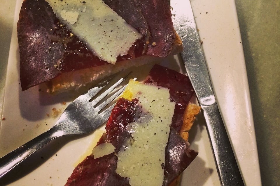 Een bord met een plak vlees, belegd met kaas en een sneetje brood.