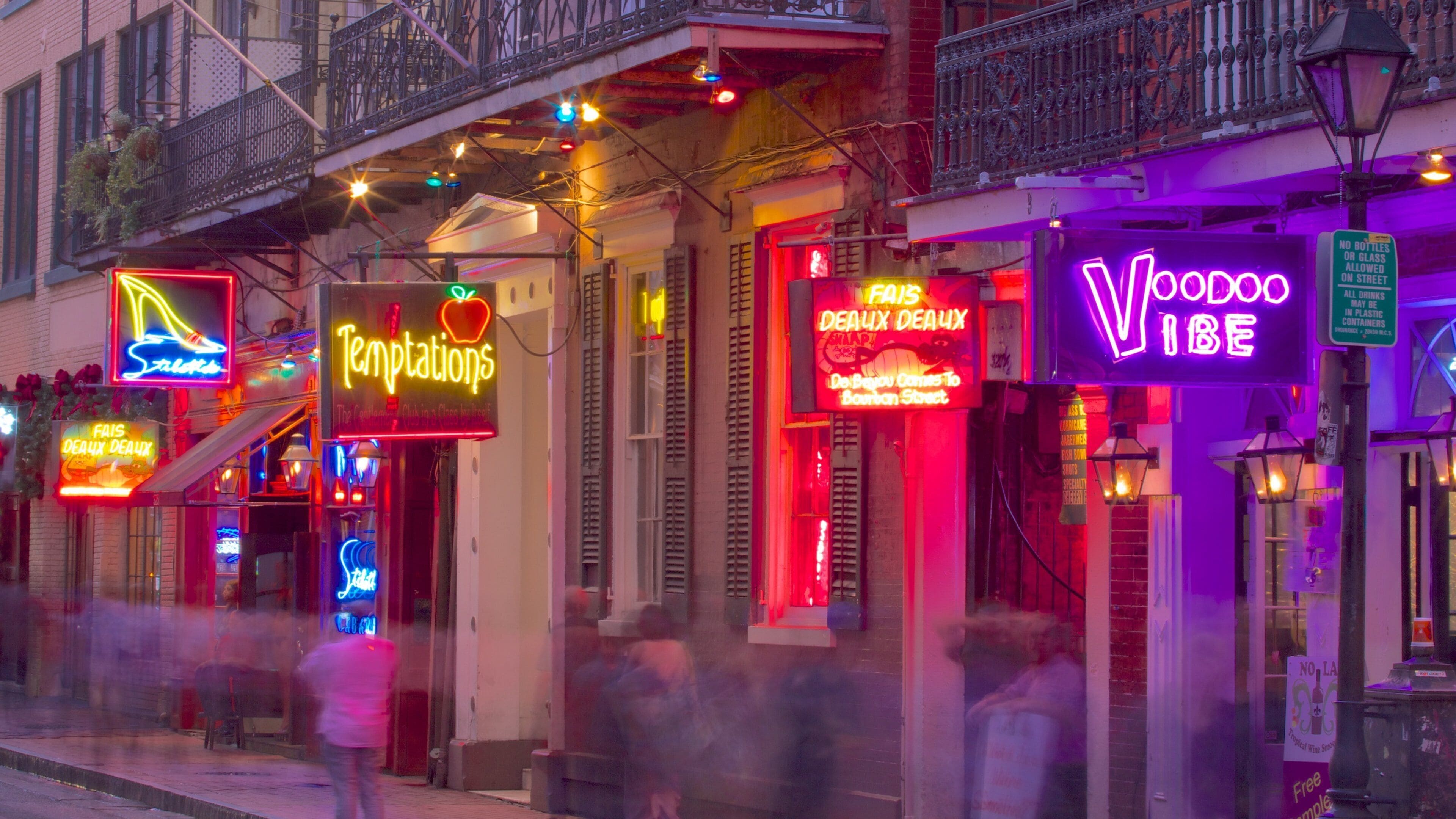 A street with brightly lit neon signs, including 'Temptations' and 'Voodoo Vibe'.