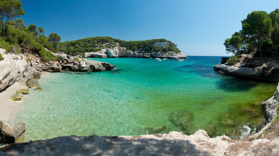A coastal landscape with clear turquoise waters, rocky cliffs, and dense greenery.