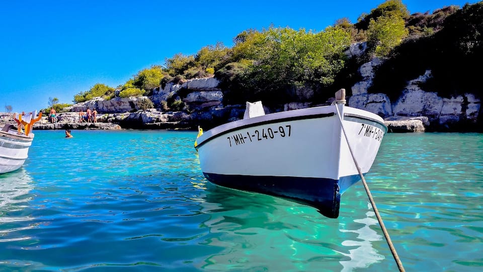 A boat with the registration number 7 MH-1-240-97 anchored near a rocky coastline with clear turquoise water.