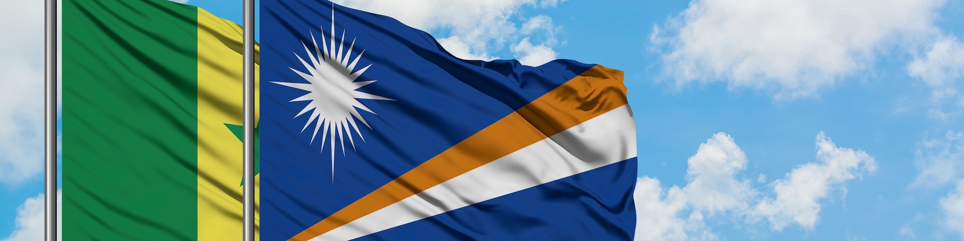 Duas bandeiras tremulando contra um céu azul com nuvens.