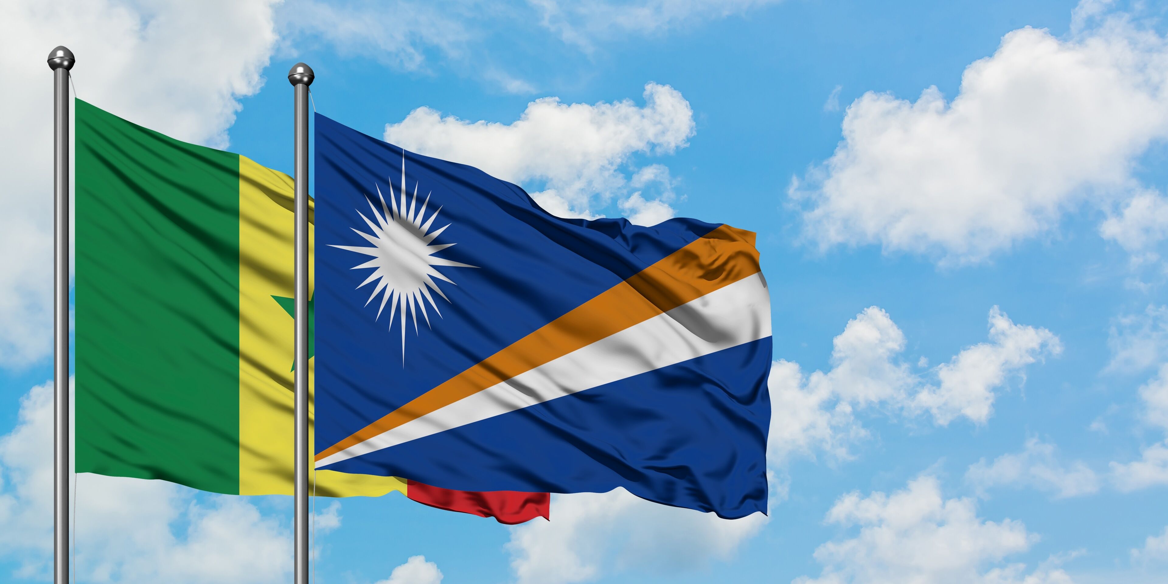 Two flags waving against a blue sky with clouds.