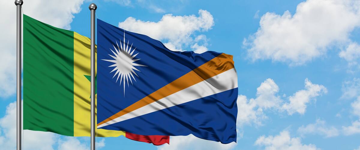 Two flags waving against a blue sky with clouds.