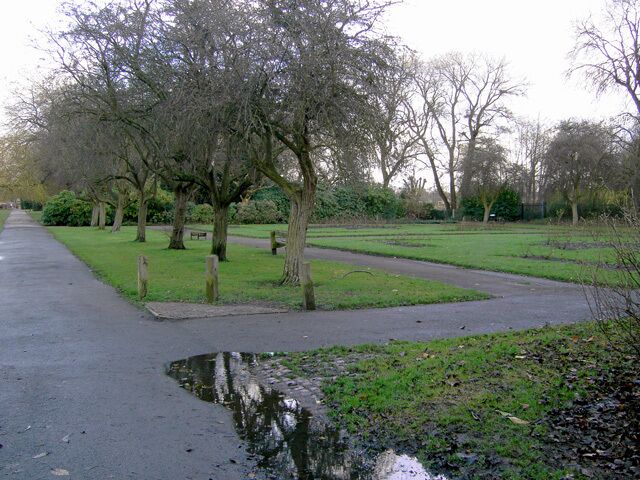 A park with a paved path, trees, and a small pond.