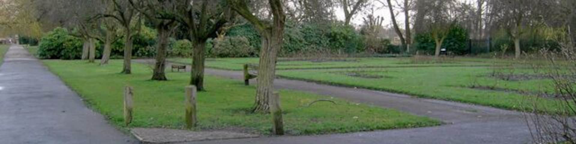 A park with a paved path, trees, and a small pond.