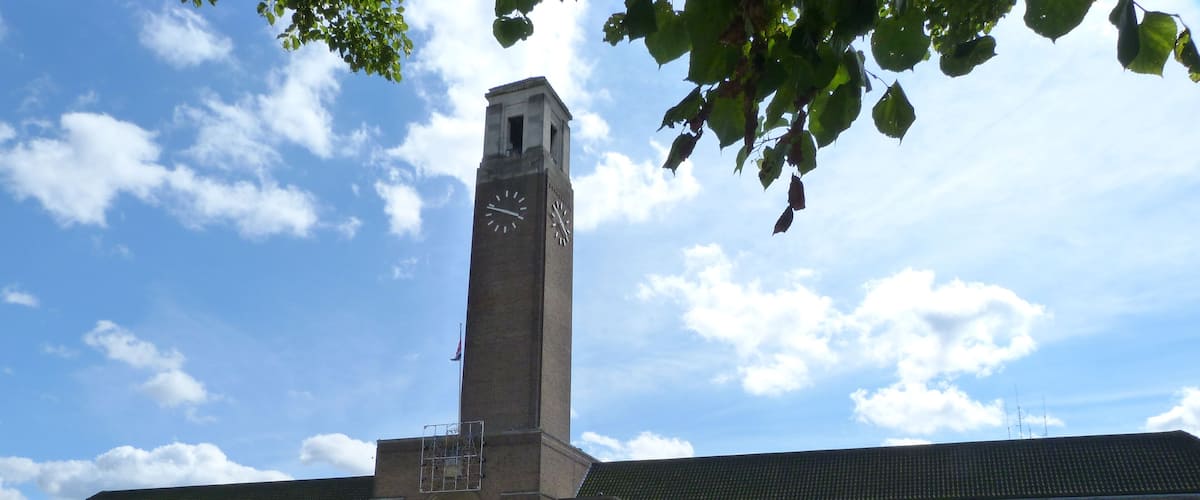 A large brick building with a clock tower, surrounded by a well-maintained lawn and flower beds.
