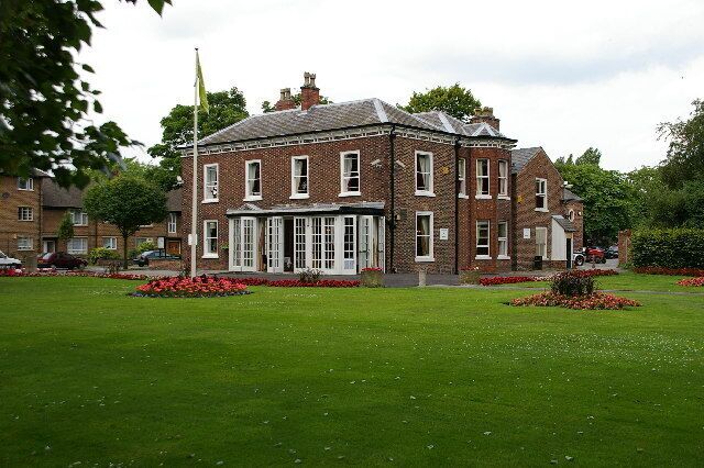 A large brick building with a central entrance, surrounded by well-maintained lawns and flower beds.