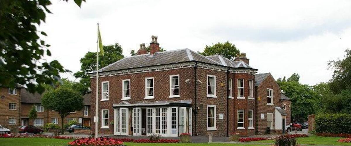 A large brick building with a central entrance, surrounded by well-maintained lawns and flower beds.