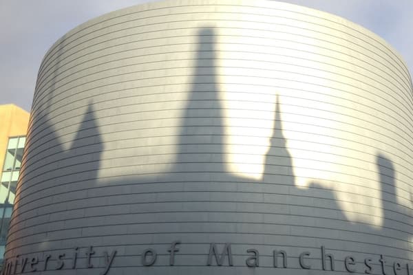 Edifício da Universidade de Manchester com fachada curva e o nome inscrito.