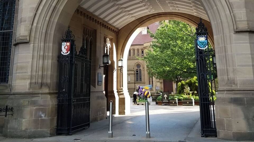 The University of Manchester's entrance with a large archway, stone facade, and a crest above the entrance.