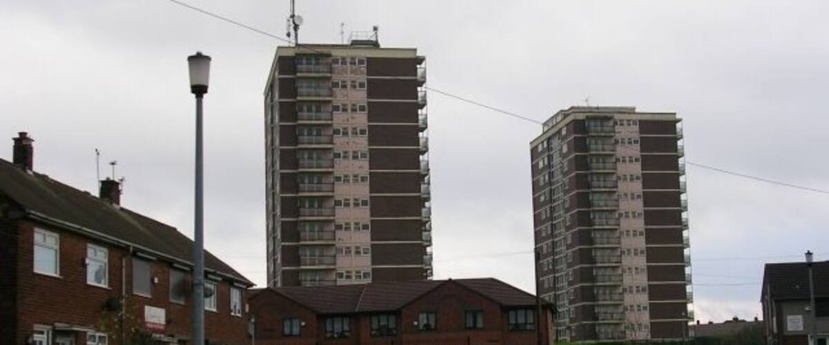 A residential area with two tall apartment buildings, a street lamp, and a green lawn.