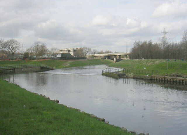 A river with a bridge, grassy banks, and a small island with a dock.