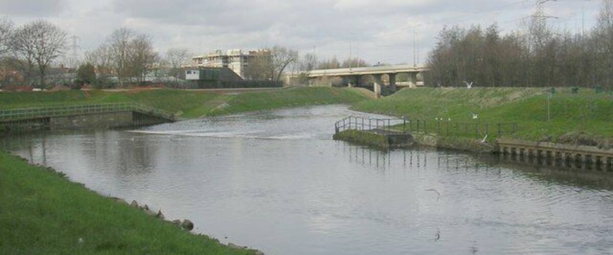 A river with a bridge, grassy banks, and a small island with a dock.