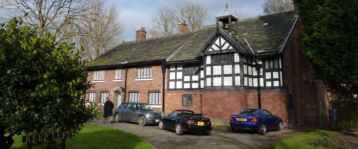 A Tudor-style house with a garden, parked cars, and a 'KEEP LEFT' sign.