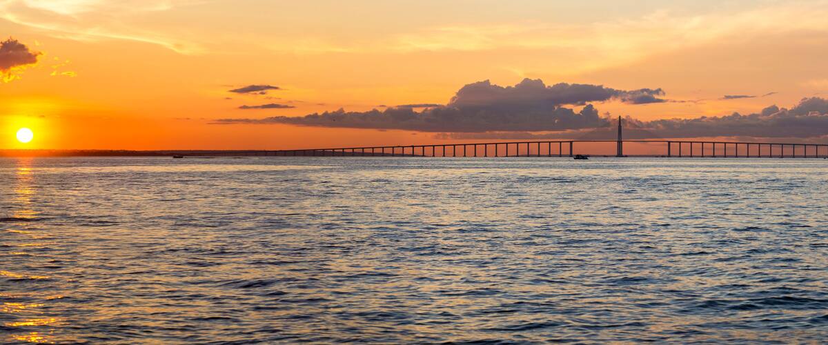 A sunset over a body of water with a bridge in the background.