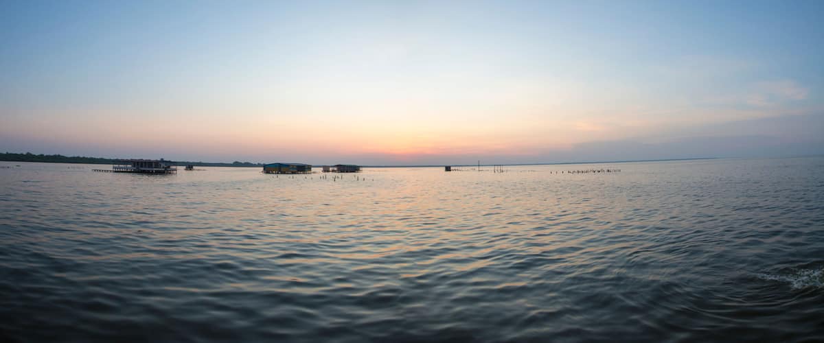 A calm lake at sunset with several small boats and a distant shoreline.