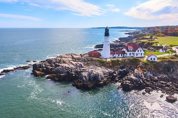 Stunning lighthouse on rocky cliffs in Maine from aerial view