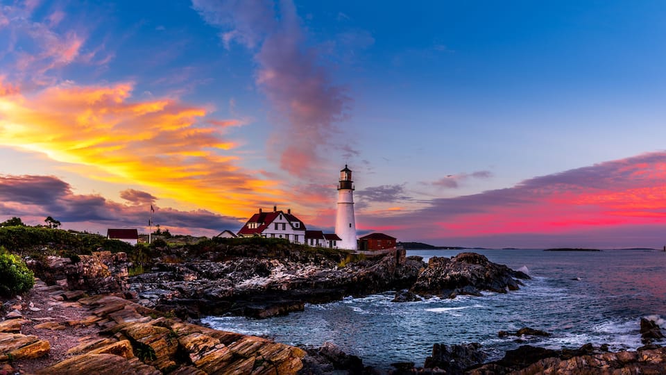 A lighthouse on a rocky coastline with a colorful sunset sky.