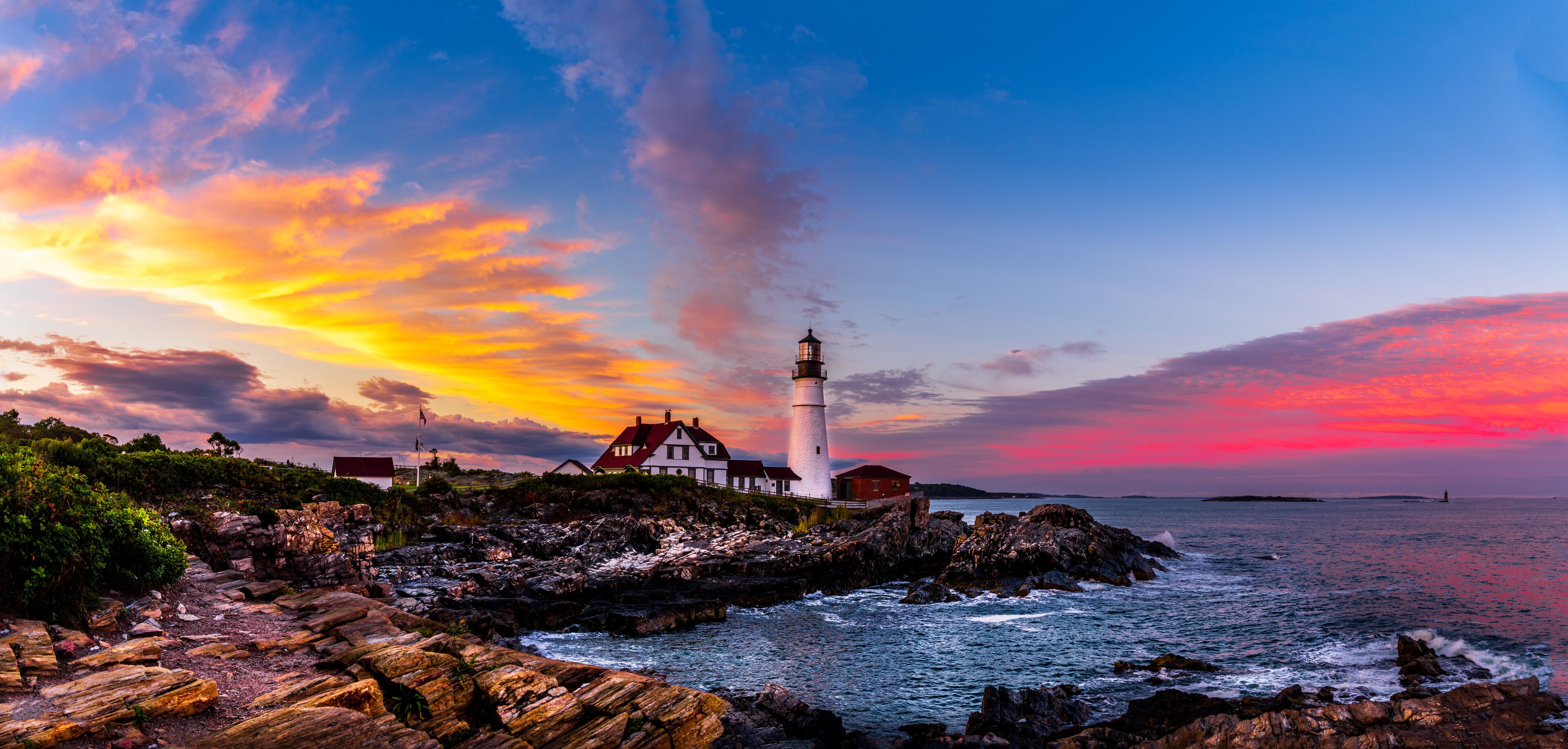 A lighthouse on a rocky coastline with a colorful sunset sky.