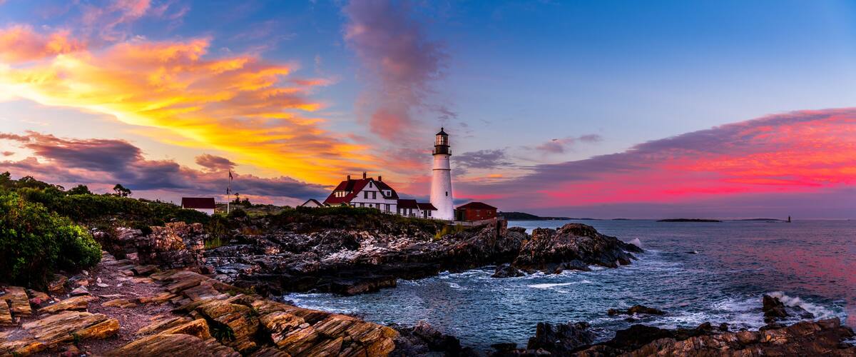 A lighthouse on a rocky coastline with a colorful sunset sky.