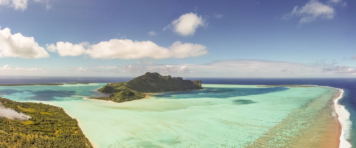 A tropical island with clear turquoise waters, a sandy beach, and lush greenery.
